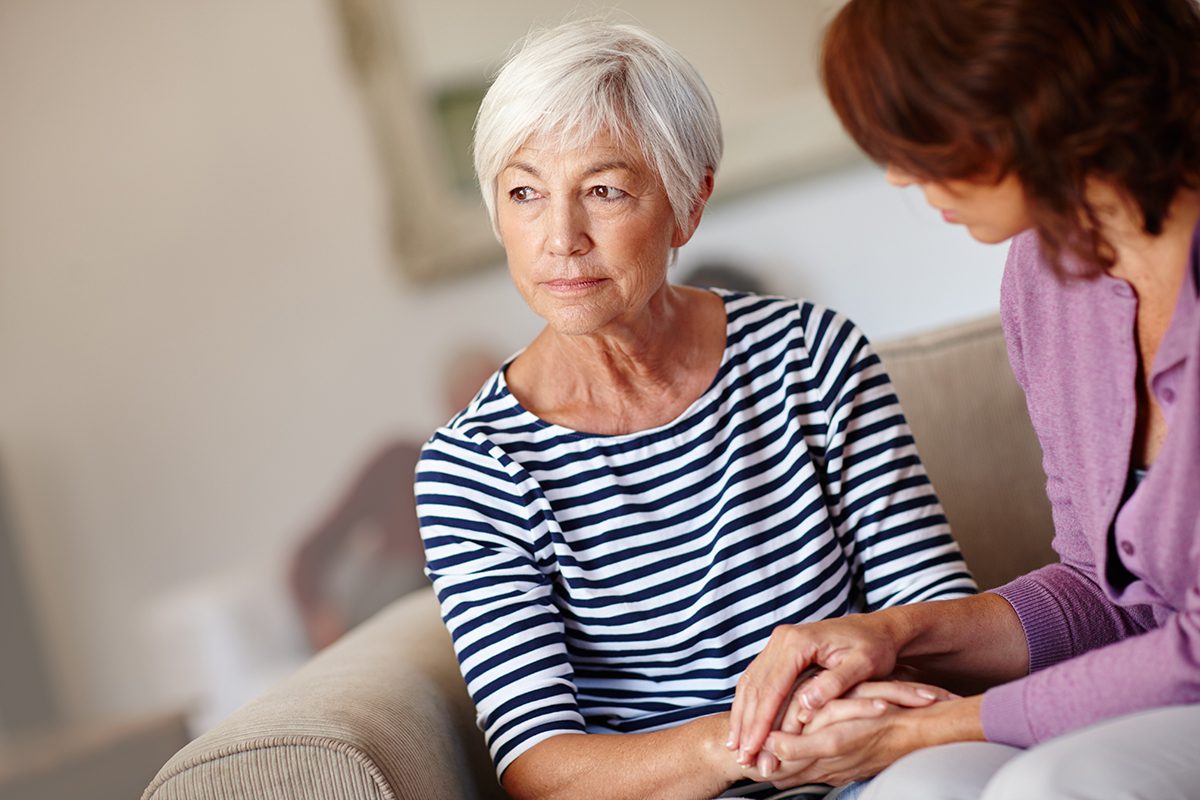 An older person who looks distressed is being comforted by another adult.