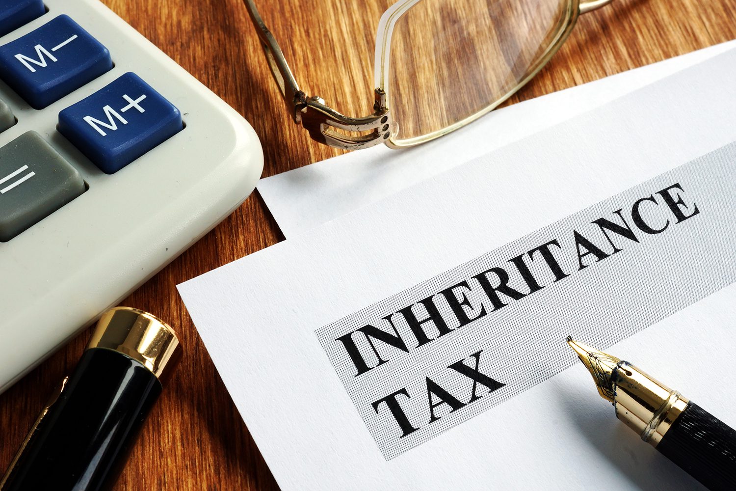 A paper with inheritance tax written on it surrounded by a calculator, pen, and glasses.